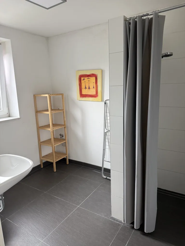 Badezimmer der Wohnung 4 mit bodenebener Dusche, Waschbecken und Regal