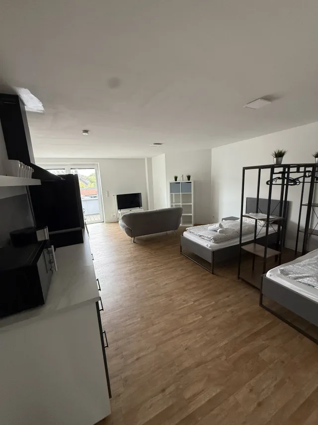 Offener Wohn-, Ess- und Küchenbereich der Wohnung 4 mit Sofa, Fernseher und zwei Einzelbetten