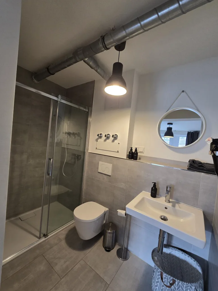 Badezimmer von Klein aber Fein mit Waschbecken, rundem Spiegel und Dusche