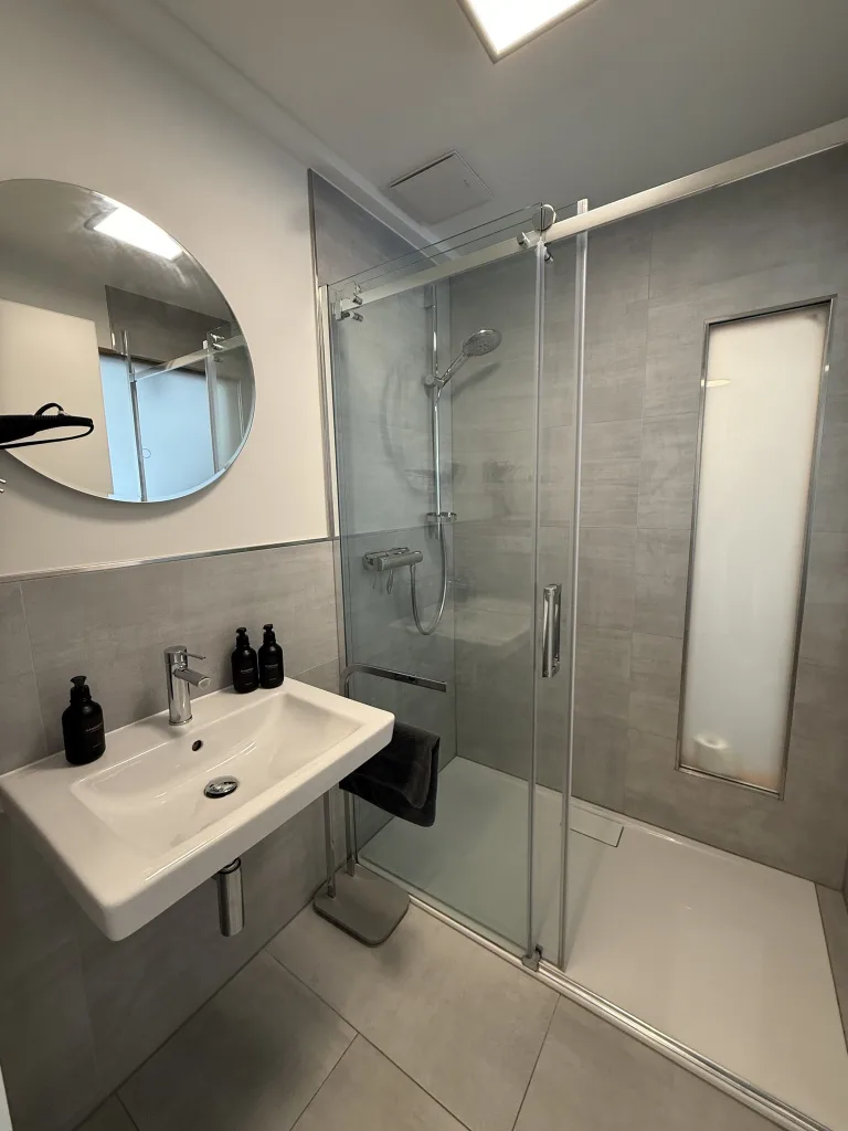 Badezimmer des Lichtnests mit Waschbecken, rundem Spiegel und Dusche