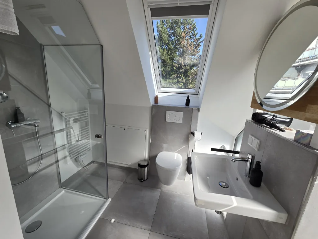 Badezimmer des Münsternests mit Dusche, Dachfenster und rundem Spiegel