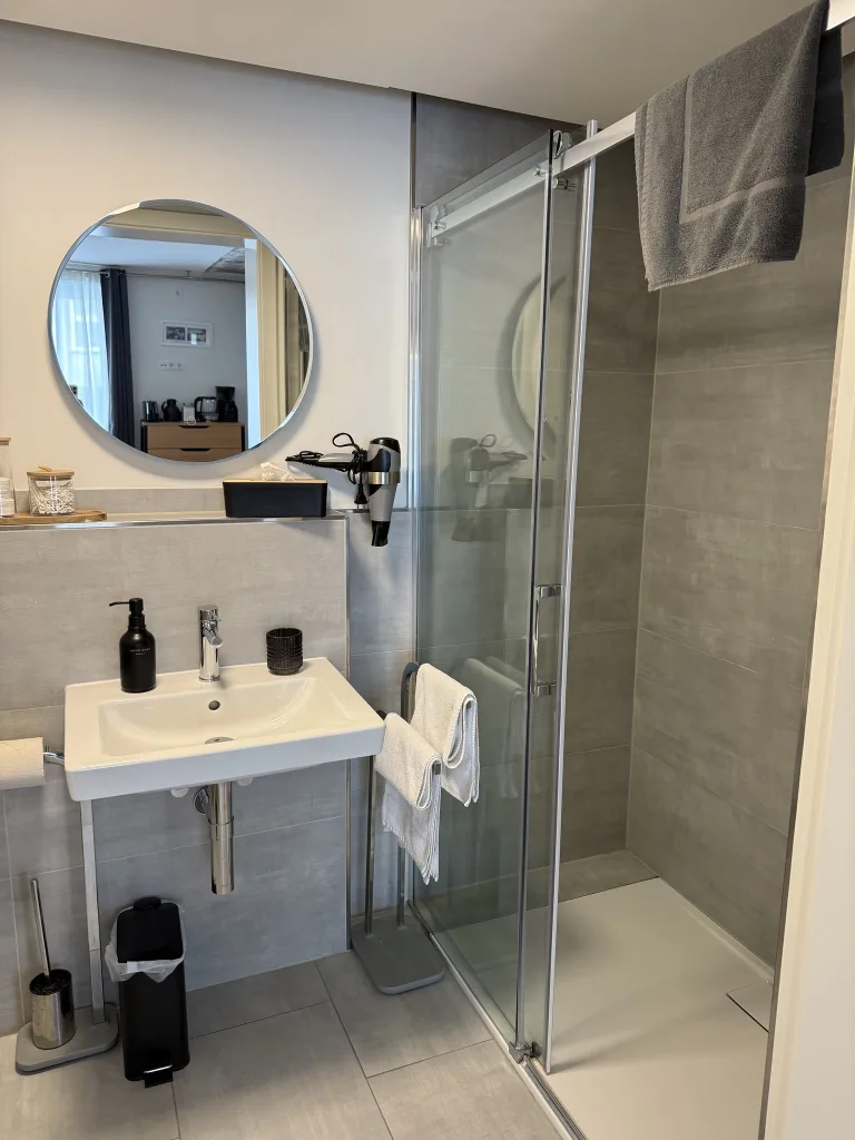 Badezimmer des Stadtfensters mit Waschbecken, rundem Spiegel und Dusche