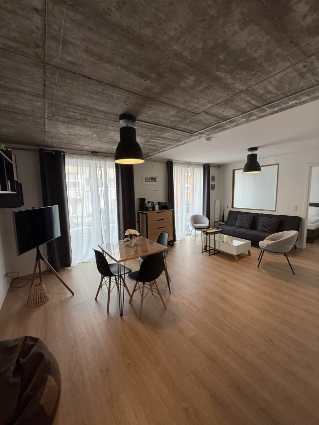 Offener Wohnbereich des Stadtfensters mit Sofa, Esstisch und Fernseher unter Betondecke