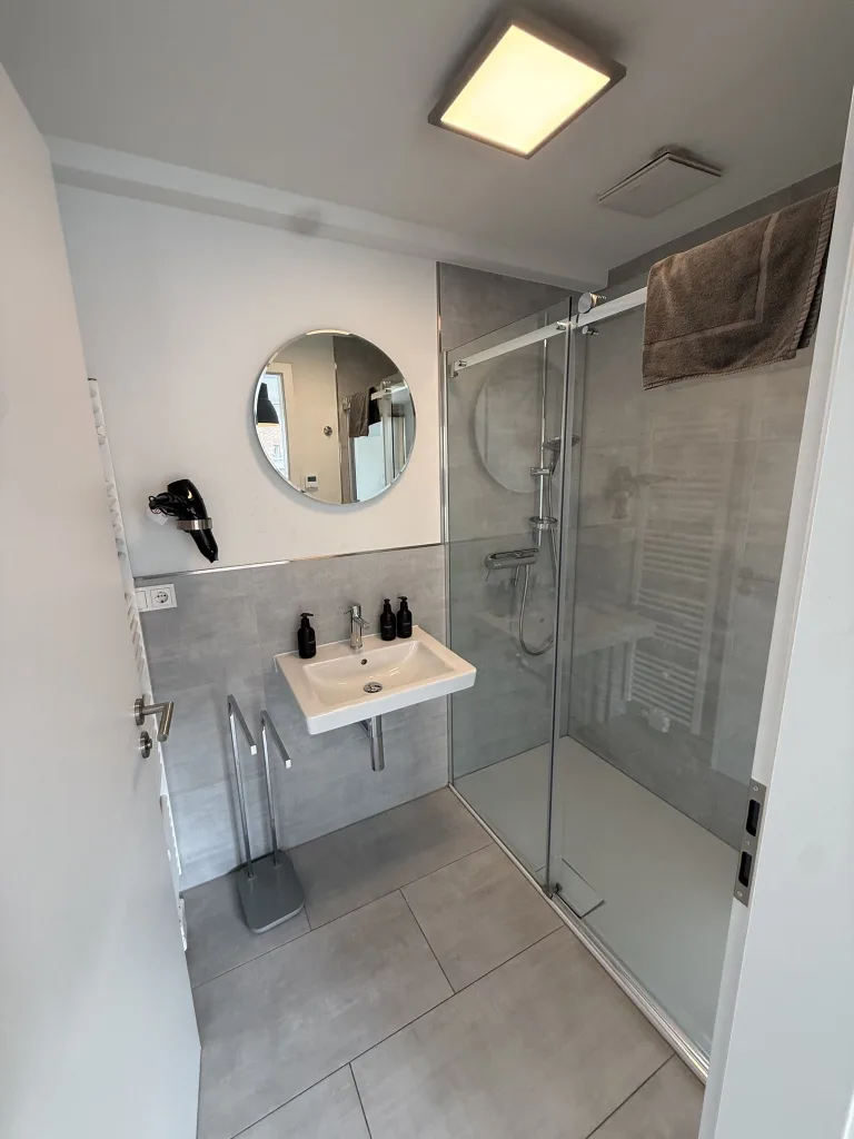 Badezimmer der Stadtruhe mit Waschbecken, rundem Spiegel und Dusche