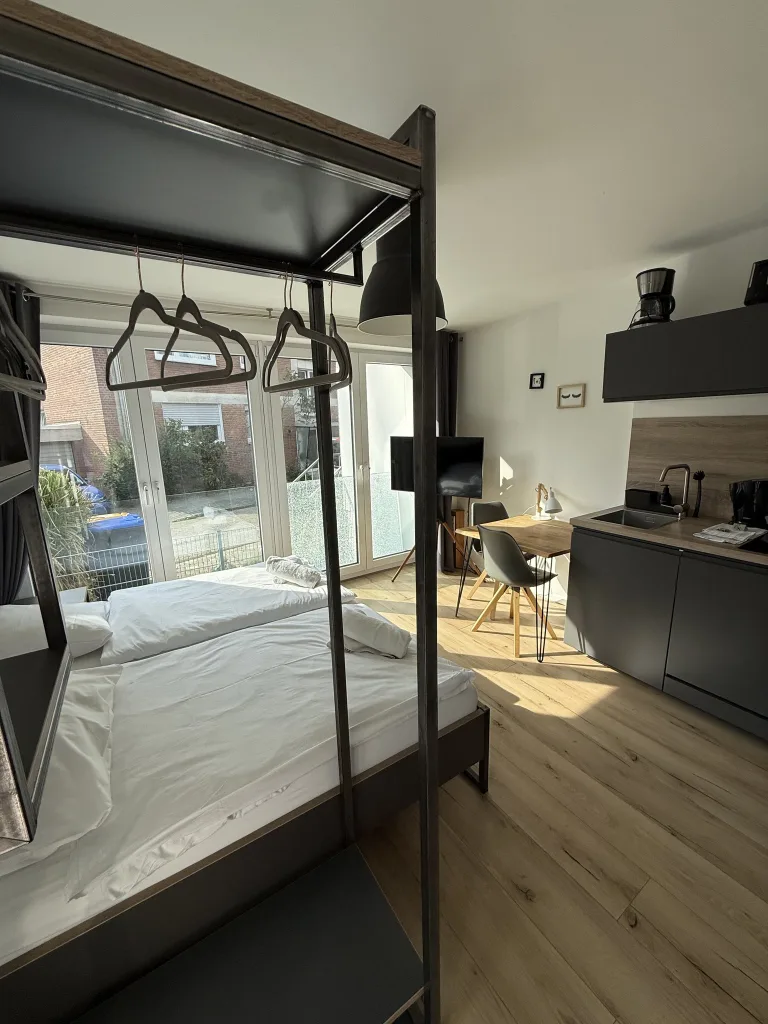 Wohnbereich der Stadtruhe mit Bett, Schreibtisch, Küchenzeile und großer Fensterfront