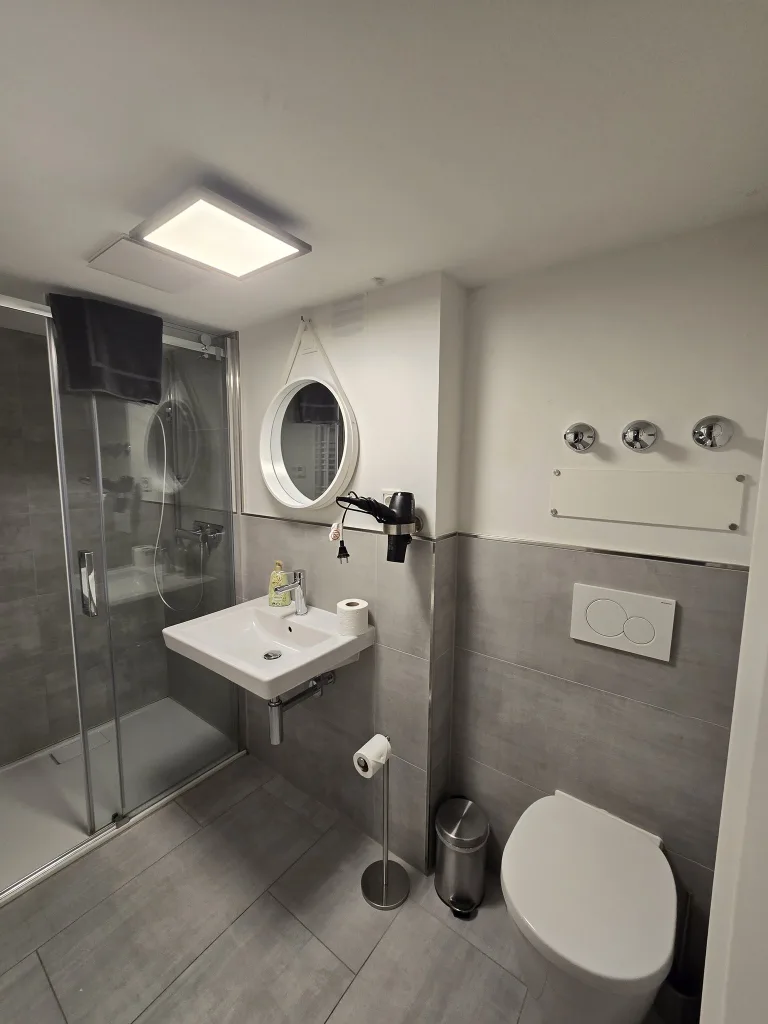 Badezimmer des Stadtverstecks mit Waschbecken, rundem Spiegel und Dusche