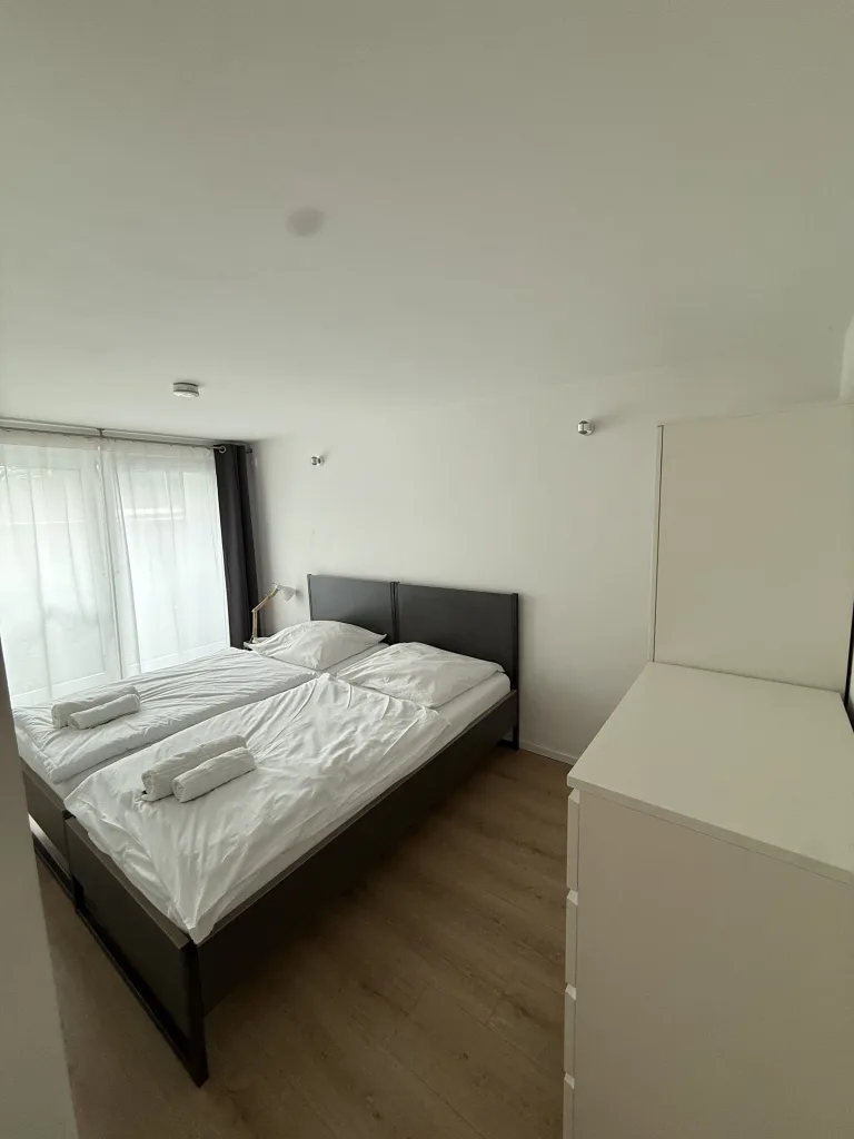 Schlafbereich des Stadtverstecks mit Doppelbett, Kommode und Fenster