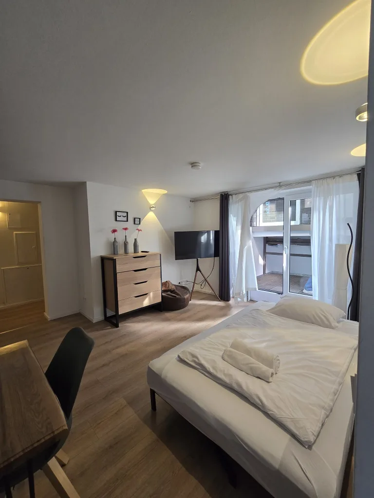Wohnbereich des Stadtverstecks mit Kommode, Fernseher und Fenster
